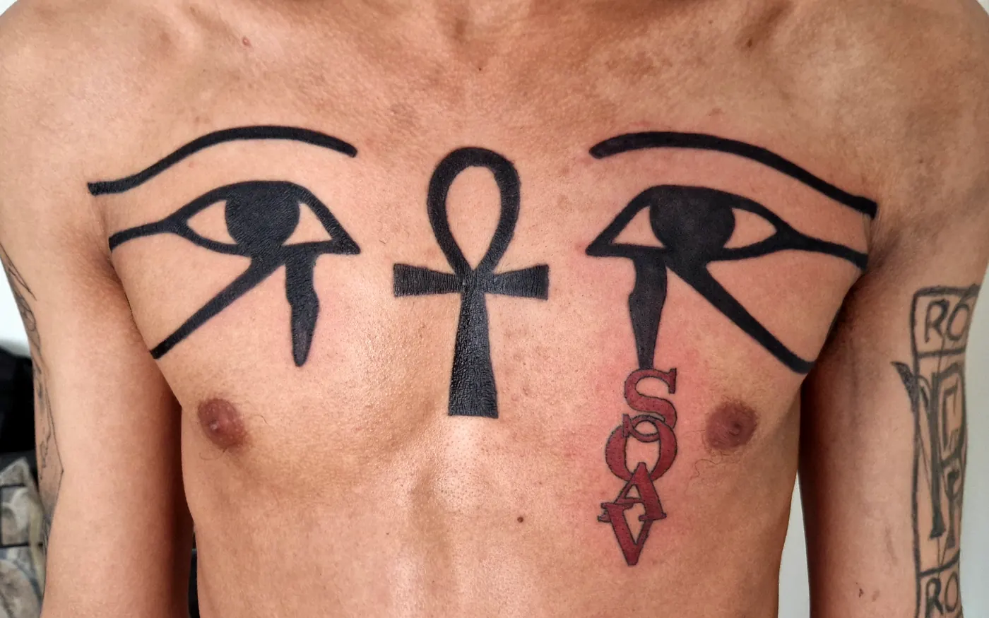 Bold eye and ankh tattoo across the chest.
